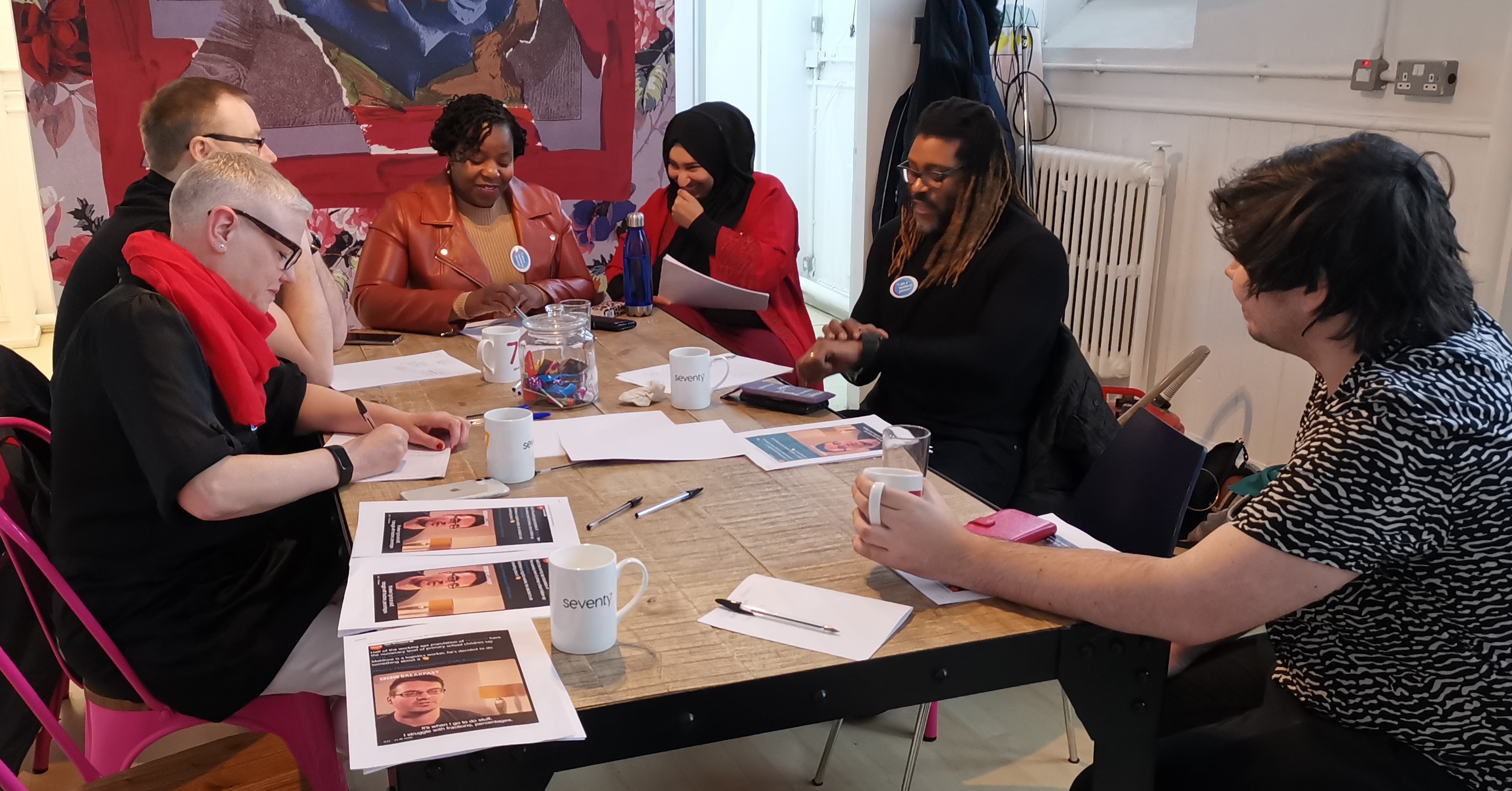Photo of the National Numeracy Day Heroes at a media training session in 2020. Six people sat around a table, engaged in conversation.