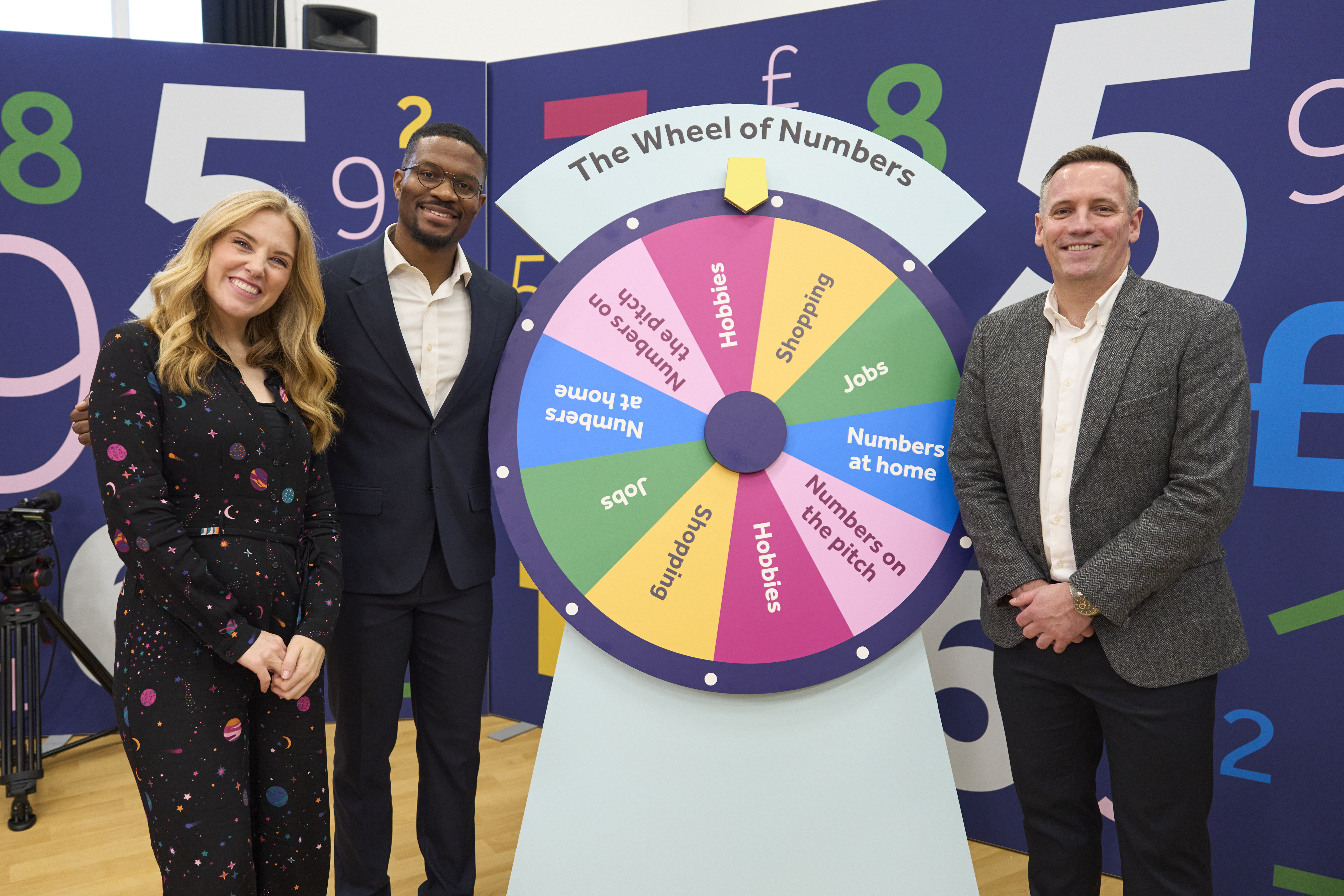 Maddie Moate, Rotimi Merriman-Johnson and Sam Sims smile next to the Wheel of Numbers