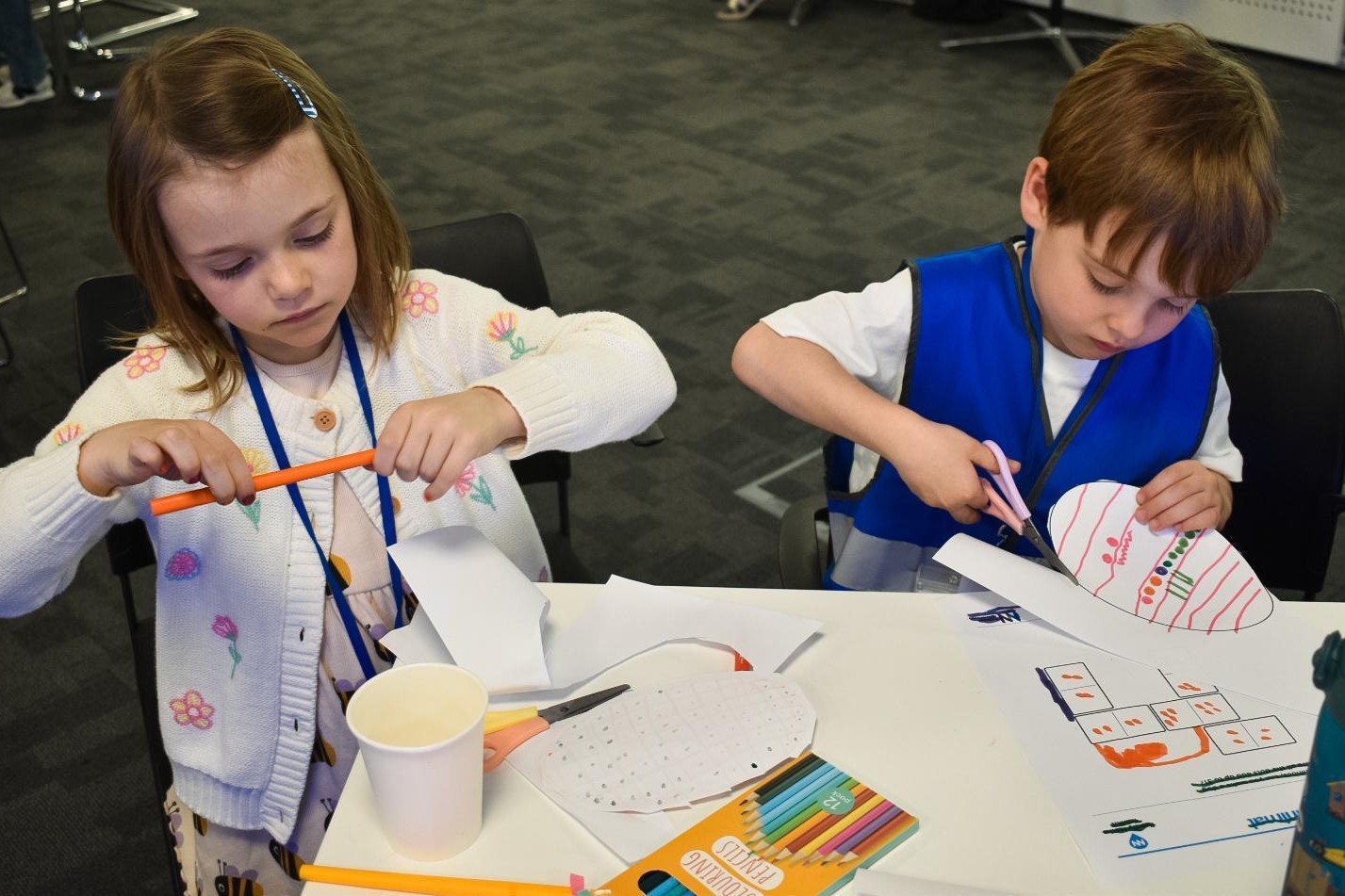Two children take part in numeracy activities, one is holding a pencil and the other is cutting around a decorated egg shape
