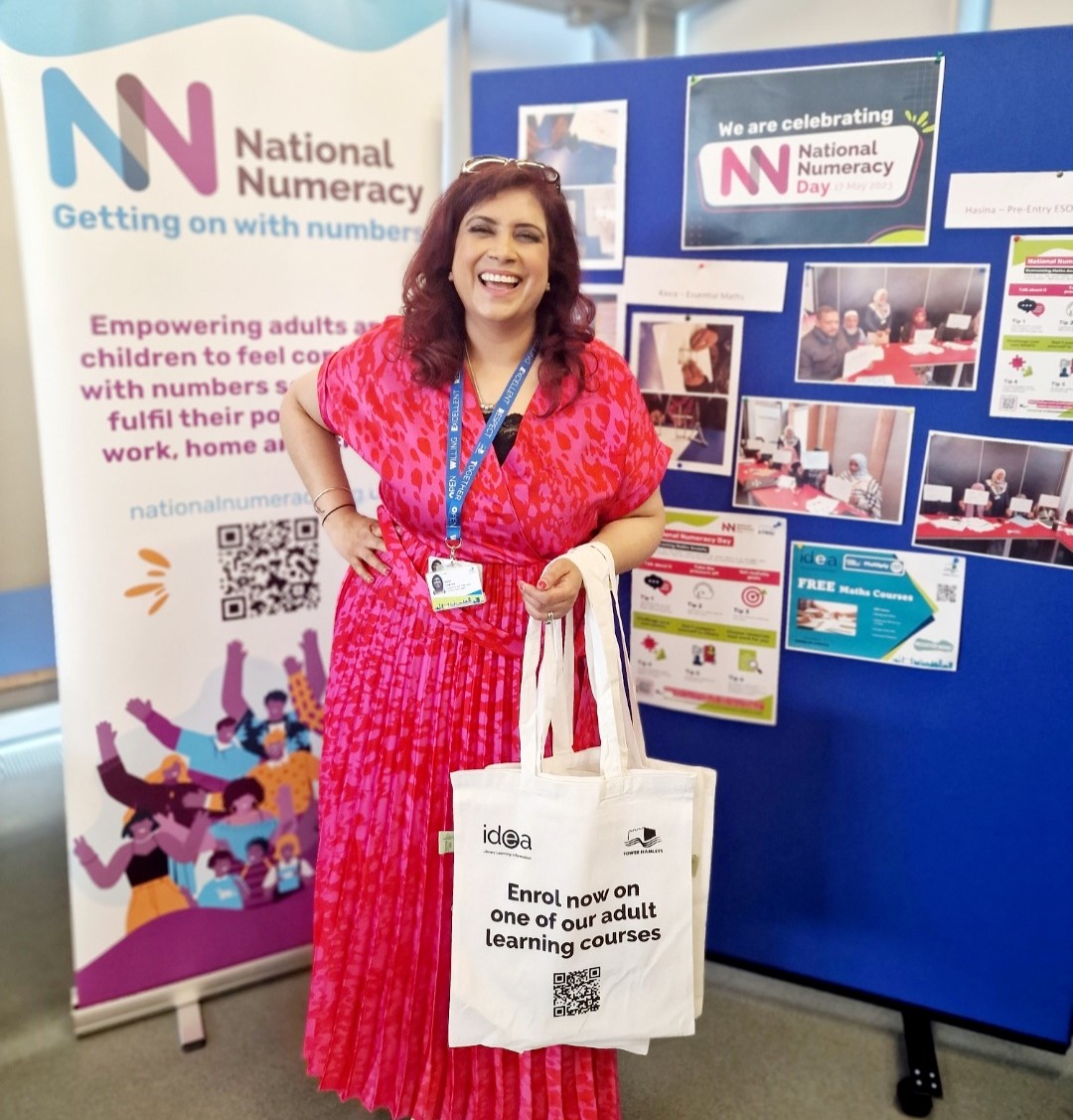 Smiling lady Nikki Chatha in front of a National Numeracy display