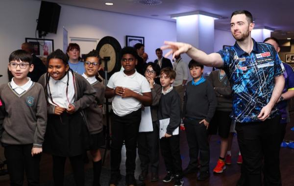 Luke Humphries throwing a dart while children watch