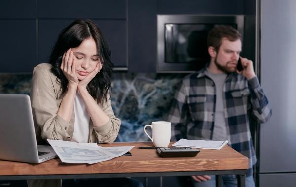 Woman stressing about bills while man stands in the background