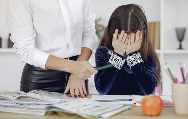 A child covering their face and looking stressed while doing homework