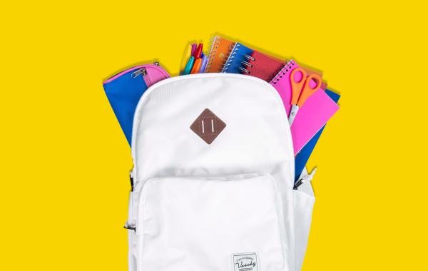 A white backpack with a pencil case, pens, notebooks and a pair of scissors coming out of the top