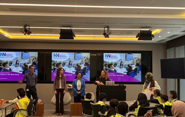 A group of school pupils listening to corporate volunteers talking abut numeracy in the workplace
