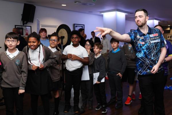 Luke Humphries throwing a dart while children watch