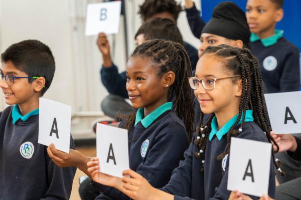 Children holding up cards during a live assembly quiz
