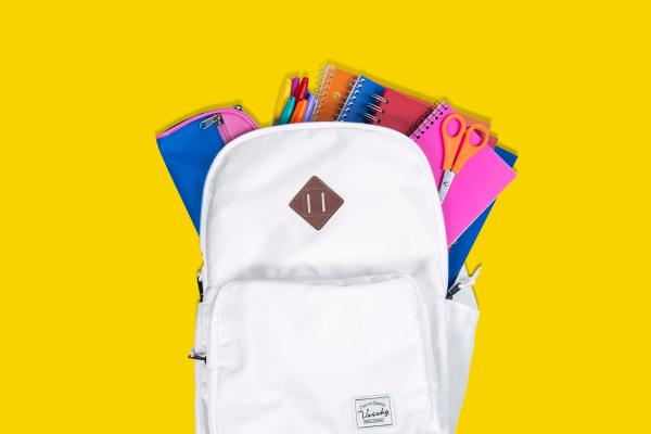 A white backpack with a pencil case, pens, notebooks and a pair of scissors coming out of the top